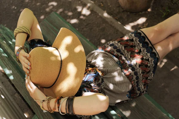 Женщина, одетая в платье и шляпу в стиле бохо, сидит на скамейке — стоковое фото