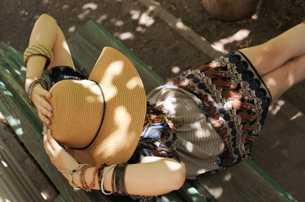 Mujer vestida con vestido y sombrero estilo boho, sentada al aire libre en un banco — Foto de Stock