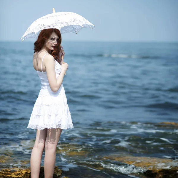 身穿白衣、头戴花边太阳伞的女孩站在海边 — 图库照片