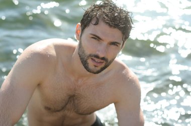 Deniz kenarında üstsüz, şık bir erkek portresi.