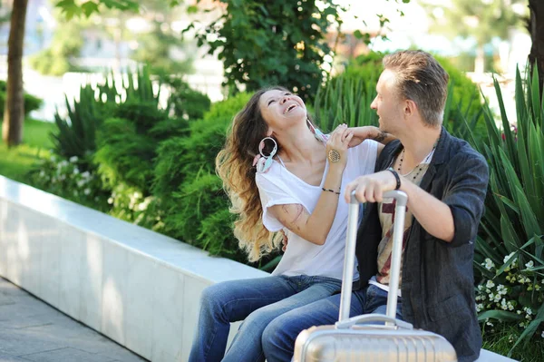 快乐的游客喜欢在户外聊天 带着手提箱坐在城市公园的长椅上 — 图库照片