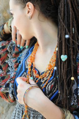 Saçları dağınık, çeşitli boncukları olan, açık havada güneşli, genç ve güzel bir kadın.