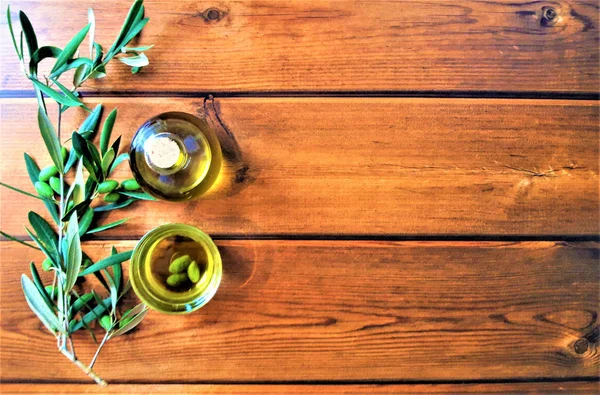 Ελαιόλαδο με ένα κλαδί από πράσινες ελιές σε φόντο ξύλινη — Φωτογραφία Αρχείου