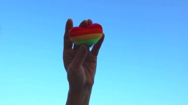 LGBT bayrağı gökkuşağı kalp şekli Lgbt gün kavramı, el mavi gökyüzüne karşı siluetli bir LGBT bayrağı gibi boyanmış bir kalp tutar