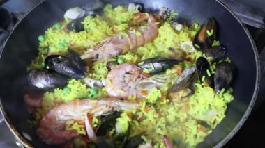 Dolly yakın bir İspanyol deniz ürünleri paella panning görünümü: midye, kral karides, langoustine, haddock. Deniz ürünleri Paella pişirme. Karides, midye ve balık ile Geleneksel İspanyol paella. Kişi taze delisious paella closeup pişirme.