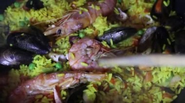 Dolly yakın bir İspanyol deniz ürünleri paella panning görünümü: midye, kral karides, langoustine, haddock. Deniz ürünleri Paella pişirme. Karides, midye ve balık ile Geleneksel İspanyol paella. Kişi taze delisious paella closeup pişirme.