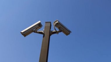 Mavi gökyüzüne karşı iki güvenlik kamerası izleniyor, uzayı kopyalıyor. Arka plan olarak mavi gökyüzüne karşı iki güvenlik kamerası 