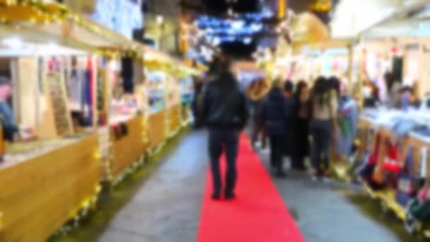 街の路上で新年のクリスマスマーケット 冬のクリスマスホリデーストリートのために美しく装飾された上を歩く歩行者のデフォーカスビュー クリスマスと新年の花輪のきらめくライトを持つ抽象的なデフォーカスビデオ — ストック動画
