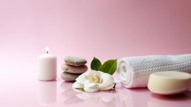 Pembe arka planda beyaz gardenya çiçeğiyle kaplıca ve spa kompozisyonu. Havlu, mumlar, çiçekler, taşlar. Masaj, oryantal terapi, refah ve meditasyon.