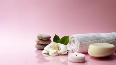 Pembe arka planda beyaz gardenya çiçeğiyle kaplıca ve spa kompozisyonu. Havlu, mumlar, çiçekler, taşlar. Masaj, oryantal terapi, refah ve meditasyon.