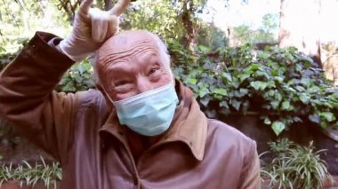 Tıbbi maskeli ve eldivenli yaşlı adam virüs önleyici 19. Son sınıf öğrencisi zafer işaretleri gösteriyor.