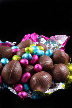 Unwrapped çikolata Paskalya yumurtaları bir siyah arka plan üzerine çevreleyen sarma renkli folyo ile yığını.