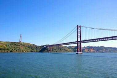 25 de Abril asma köprüsü Lizbon şehrini Almada belediyesine bağlıyor ve arka plandaki İsa heykeli Tejo Estuary, Lizbon, Portekiz 'in güney kıyılarının üzerinde duruyor..