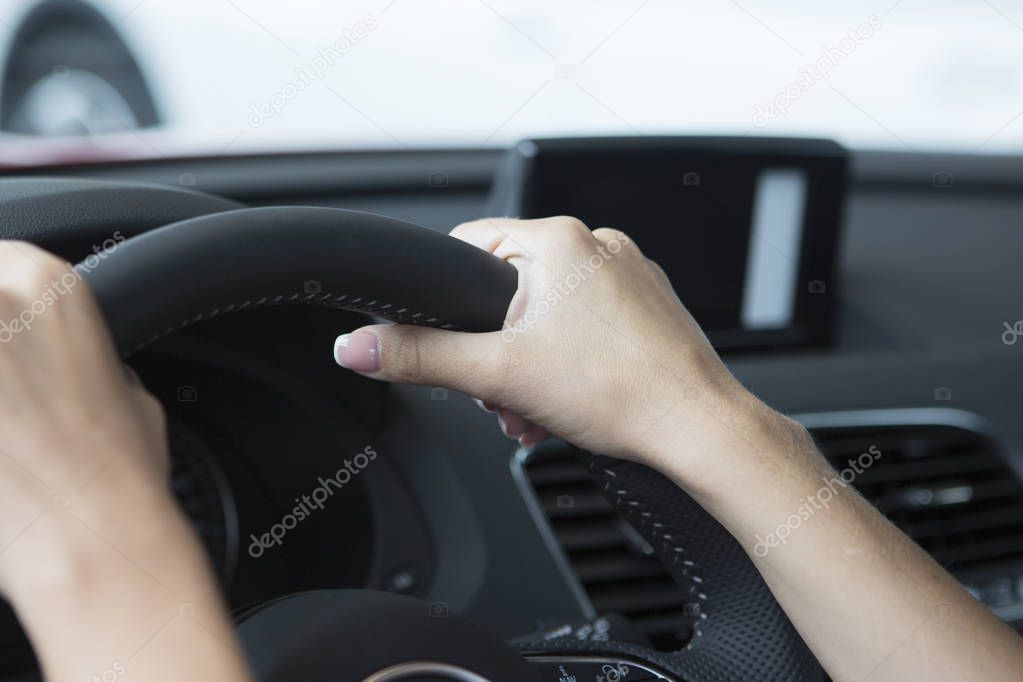 The hand of a girl with a stylish manicure lies on the handlebars in a saloon car. Close-up