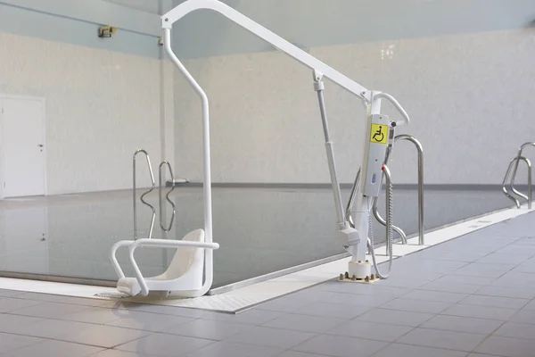 Lift for the descent of people with disabilities into the pool. On a blurred background, a swimming pool is visible