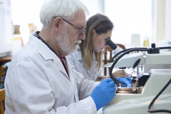 Health care researchers working in life science laboratory. Young female research scientist and senior male supervisor preparing and analyzing microscope slides in research lab.