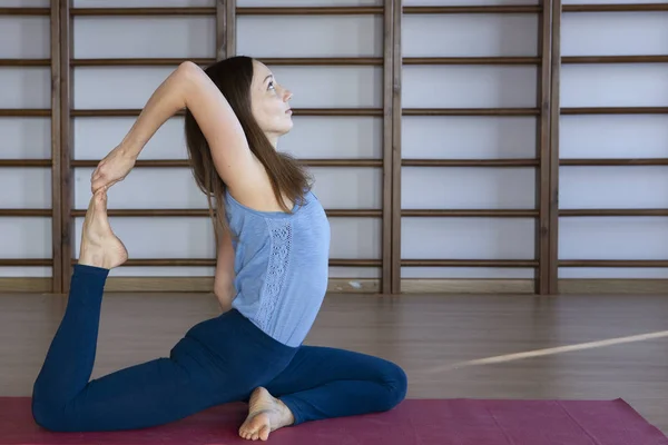 Joven mujer atractiva deportiva practicando yoga, haciendo ejercicio de sirena, pose de Eka Pada Rajakapotasana, haciendo ejercicio, usando ropa deportiva, pantalones y top, de cuerpo entero, estudio de yoga — Foto de Stock