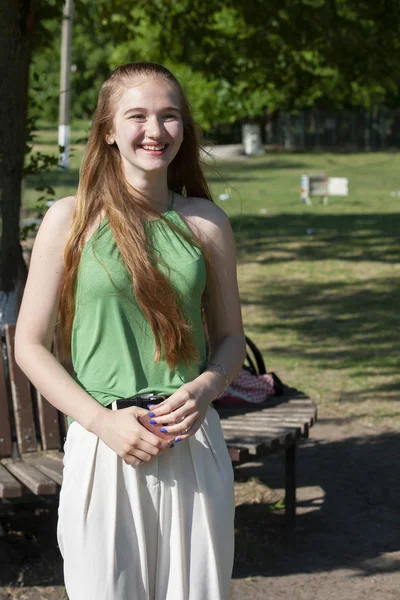 Hermosa joven con ojos azules sobre un fondo verde. Mujer joven Wistful en una calle en un parque en el fondo . — Foto de Stock