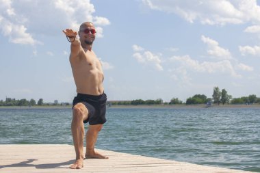 Genç adam yoga yapıyor ve savaşçı sahilde poz meditasyon
