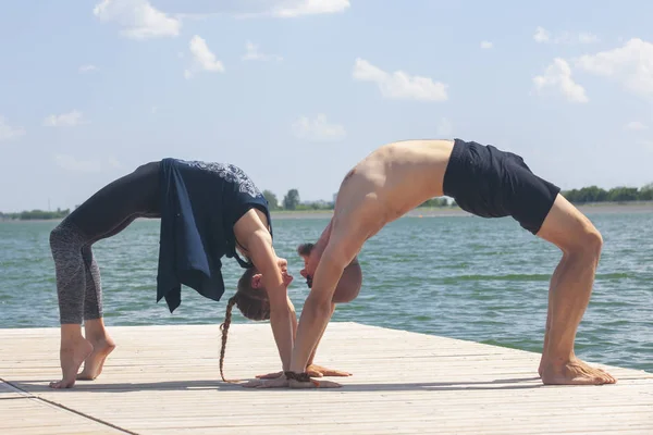 Genç bir adam ve bir kadın, güneşli bir yaz günü, göl kenarında yoga yapıyorlar.