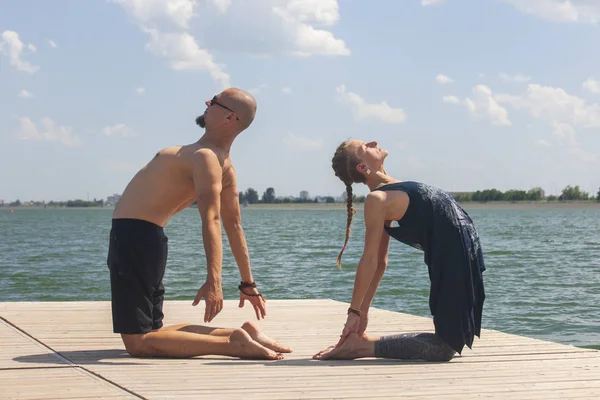 Genç bir adam ve bir kadın, güneşli bir yaz günü, göl kenarında yoga yapıyorlar.