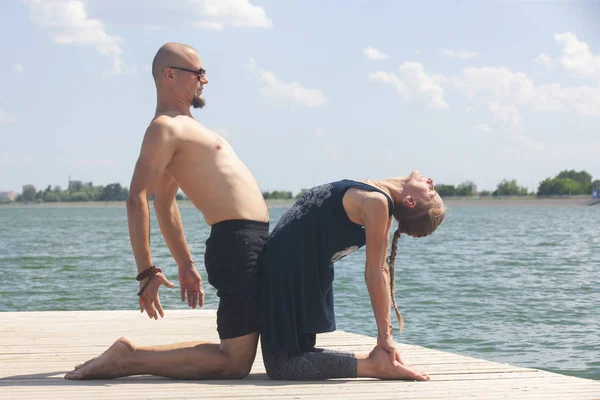Genç bir adam ve bir kadın, güneşli bir yaz günü, göl kenarında yoga yapıyorlar.