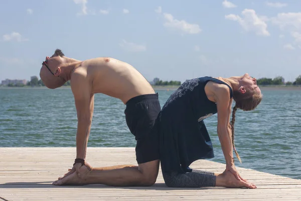Genç bir adam ve bir kadın, güneşli bir yaz günü, göl kenarında yoga yapıyorlar.