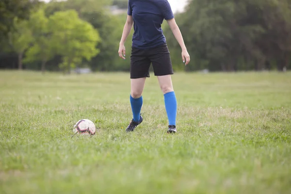 Jovem futebolista ou jogadora de futebol feminino com cabelo comprido em sportwear e botas chutando bola para o gol no salto no estádio . — Fotografia de Stock