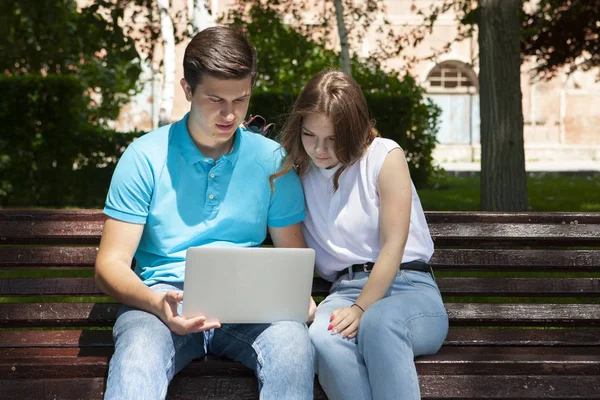 Feliz jovem casal usando laptop computador sentado no banco em cit — Fotografia de Stock