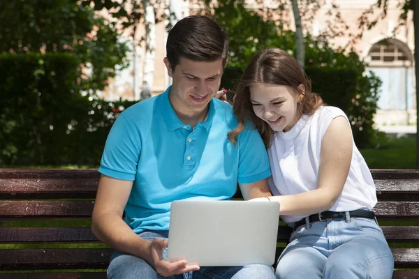 Feliz joven pareja usando ordenador portátil sentado en el banco en cit — Foto de Stock