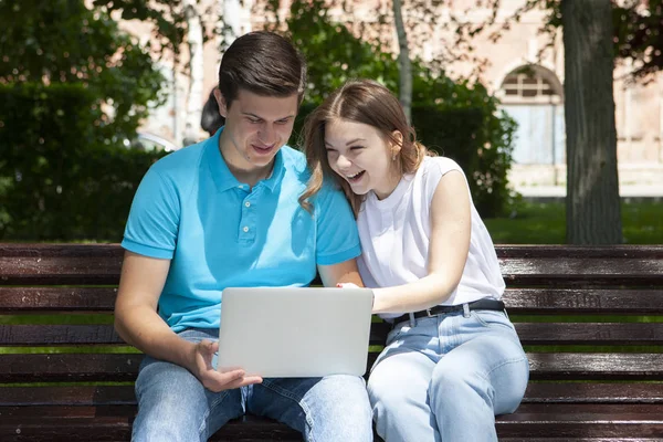 Glückliches junges Paar sitzt mit Laptop-Computer auf Bank in cit — Stockfoto