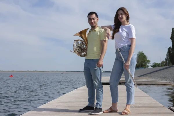 O tipo a tocar trompa e a rapariga a tocar flauta no lago. — Fotografia de Stock