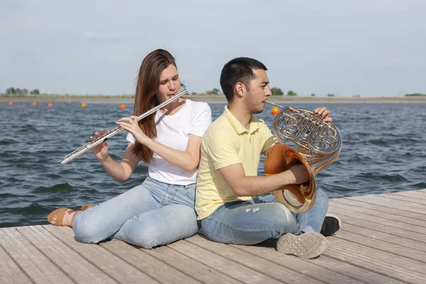 O tipo a tocar trompa e a rapariga a tocar flauta no lago. — Fotografia de Stock