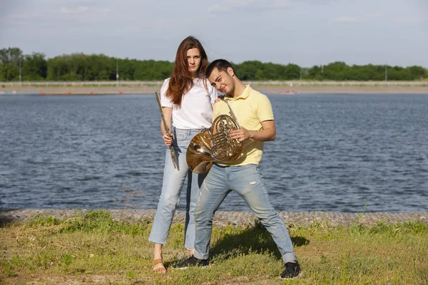 O tipo a tocar trompa e a rapariga a tocar flauta no lago. — Fotografia de Stock