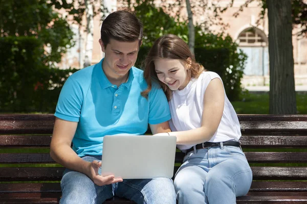 Feliz joven pareja usando ordenador portátil sentado en el banco en cit — Foto de Stock