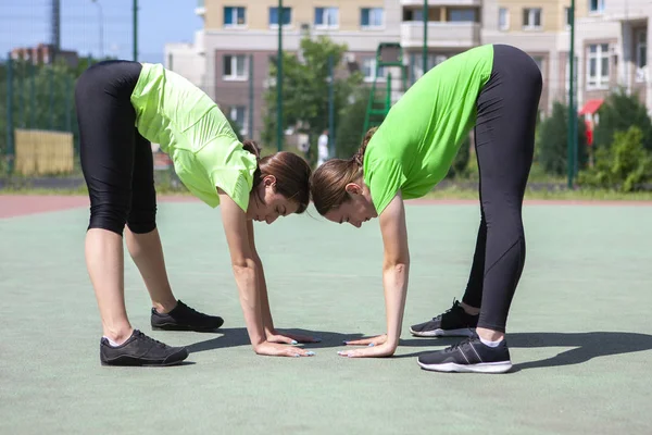 Two beautiful women stretching in city park after running and sport activity