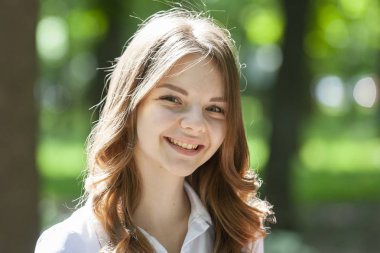 Kısa sarı saçlı muhteşem kız parkta yürüyor. Sevimli kız mutlu görünüyor ve gülümsüyor.