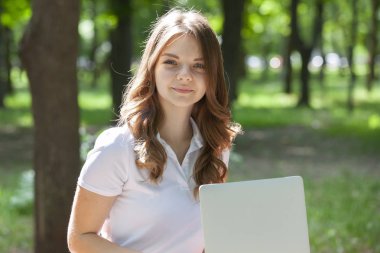 Parkta dizüstü bilgisayar kullanan güzel bir genç kadın..