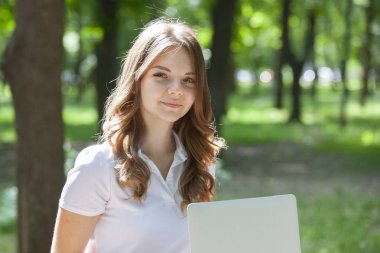 Parkta dizüstü bilgisayar kullanan güzel bir genç kadın..
