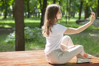 Güneşli bir günde bir parkta bir bankta oturan bir akıllı telefon ile güzel neşeli kız