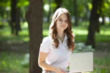 Parkta dizüstü bilgisayar kullanan güzel bir genç kadın..