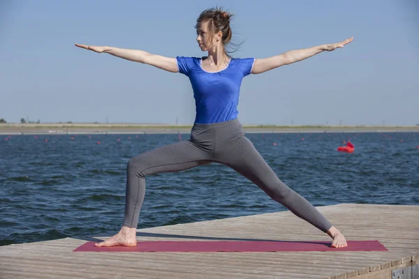 Stile di vita sano in natura, Donna che fa esercizio di yoga sul tappeto nel parco vicino al lago . — Foto Stock