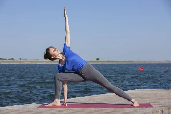 Stile di vita sano in natura, Donna che fa esercizio di yoga sul tappeto nel parco vicino al lago . — Foto Stock