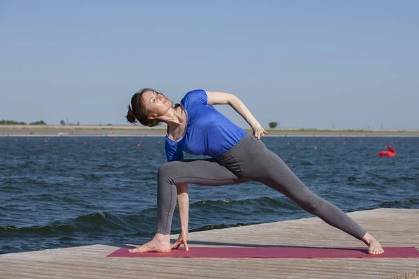 Stile di vita sano in natura, Donna che fa esercizio di yoga sul tappeto nel parco vicino al lago . — Foto Stock