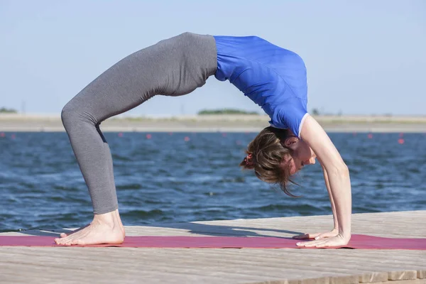 Schöne kaukasische Frau übt Yoga in der Natur neben einem See — Stockfoto