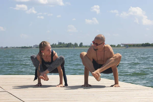 Athletic strong couple practicing difficult yoga pose outdoors