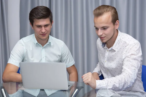 Dos jóvenes empresarios alegres que trabajan y utilizan el ordenador portátil en la reunión de negocios juntos — Foto de Stock