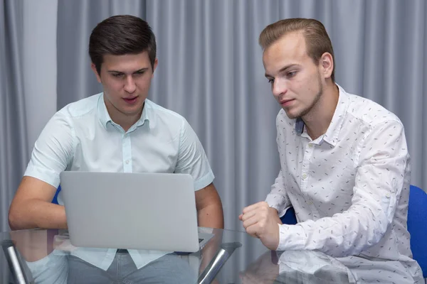 Dos jóvenes empresarios alegres que trabajan y utilizan el ordenador portátil en la reunión de negocios juntos — Foto de Stock