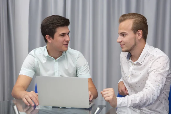 Zwei gut gelaunte junge Geschäftsleute, die zusammen an einem Geschäftstreffen arbeiten und Laptop benutzen — Stockfoto