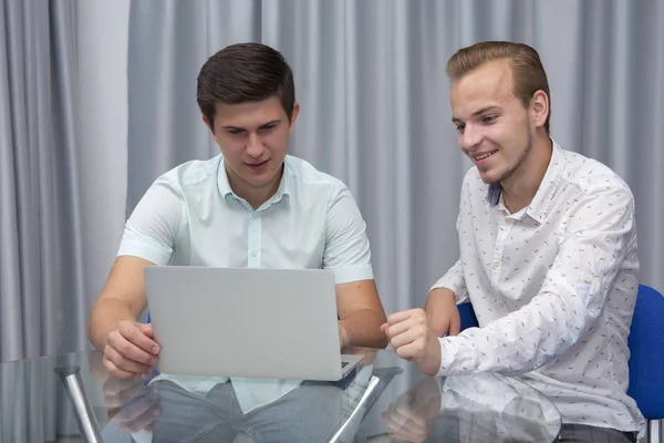 Dos jóvenes empresarios alegres que trabajan y utilizan el ordenador portátil en la reunión de negocios juntos — Foto de Stock